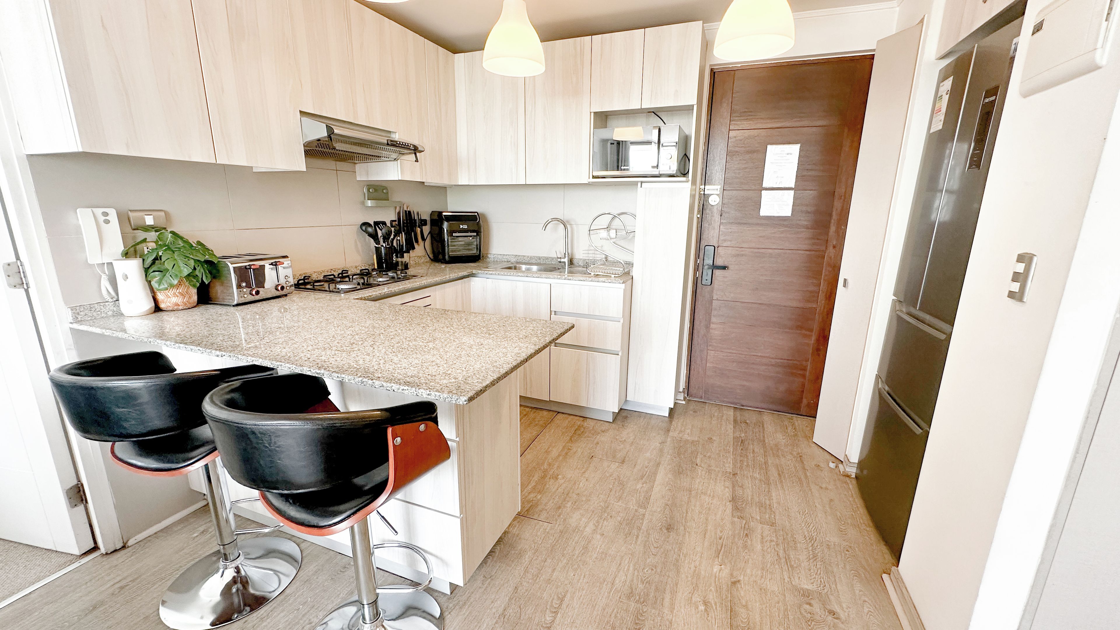 A modern kitchen with a central island, bar stools, a microwave, and a refrigerator.
