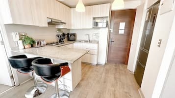 A modern kitchen with a central island, bar stools, a microwave, and a refrigerator.