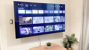 Un televisor de pantalla plana montado en la pared que muestra una interfaz de servicio de transmisión con varios iconos de aplicaciones y una sección 'Reproducir siguiente'.