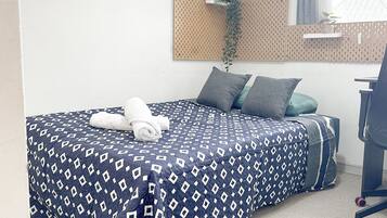 Una cama bien tendida con una colcha estampada, dos almohadas y una toalla blanca enrollada.