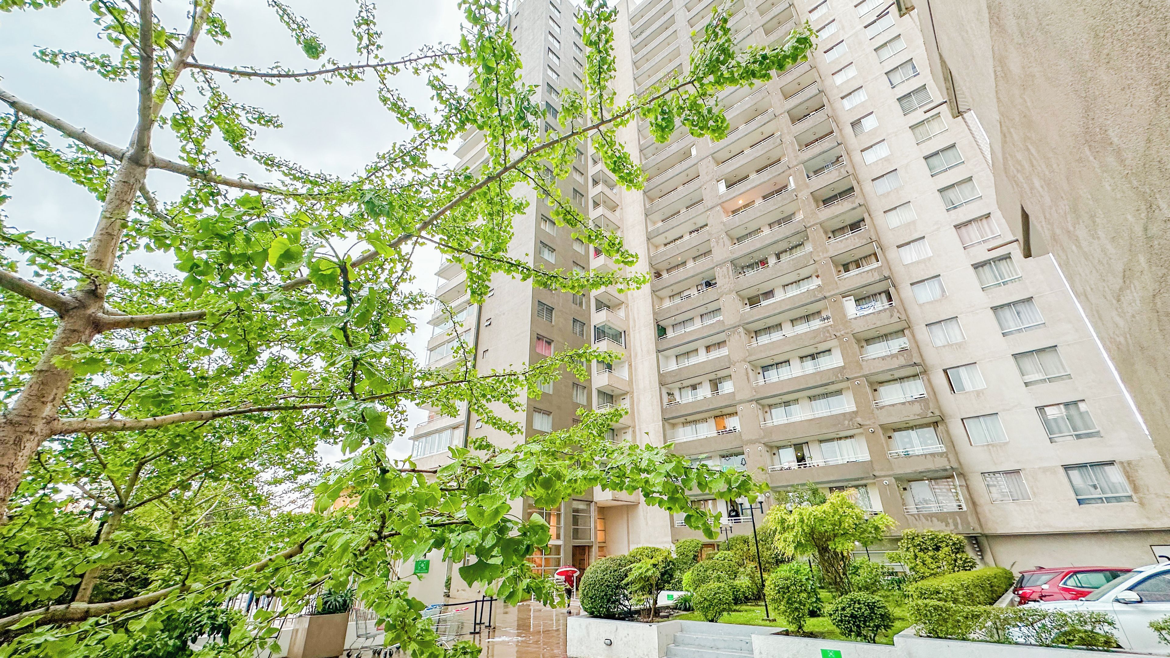 Un edificio residencial alto con varios balcones, una entrada protegida por un muro y un jardín bien cuidado.