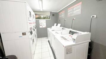 Un cuarto de lavandería con varias lavadoras y secadoras, terminales de pago y carteles informativos en las paredes.