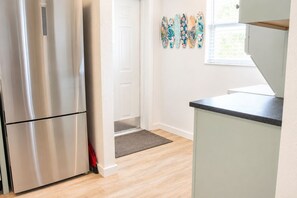 A kitchen with a stainless steel refrigerator, a white door, a small rug, and surfboard decorations on the wall. - Downtown Venice Island | private patio, walkable (Venice)