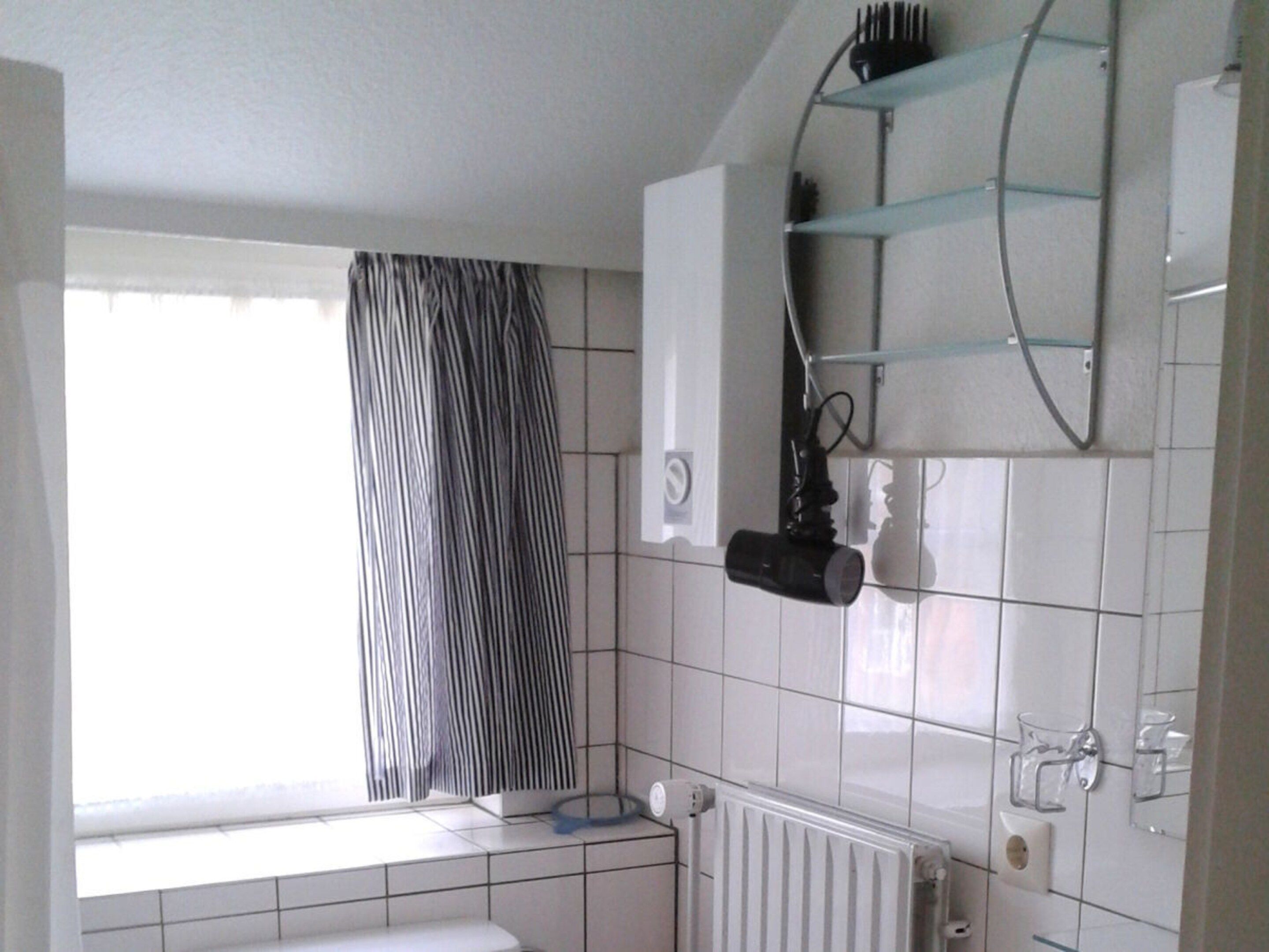 A bathroom with a window, a radiator, a towel rack, and a mirror.