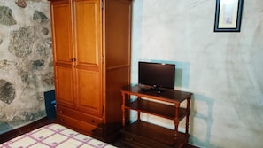 Une pièce avec une armoire en bois, un téléviseur posé sur un meuble en bois et un mur en pierre.