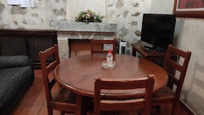 Taula de dinar rodona de fusta amb sis cadires, una làmpada de taula petita i un arranjament floral sobre una alçada de llar de pedra.