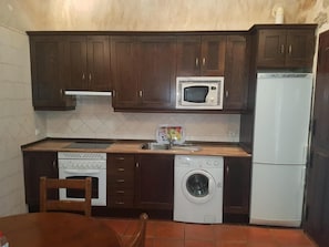 Une cuisine compacte avec des meubles de rangement en bois foncé, un four à micro-ondes, une cuisinière, un lave-linge et un réfrigérateur.