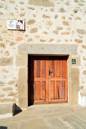 Un mur de pierres rustiques, avec une porte en bois et une enseigne indiquant qu’il s’agit d’une maison de campagne.