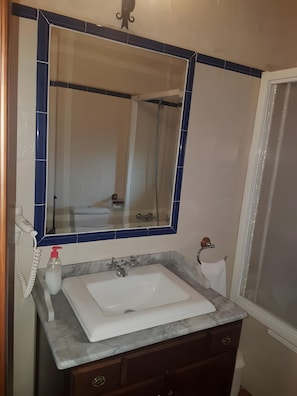 Un bany amb un lavabo blanc, un mirall amb marc blau, un assecador de cabells de mà i una ampolla de sabó líquid.