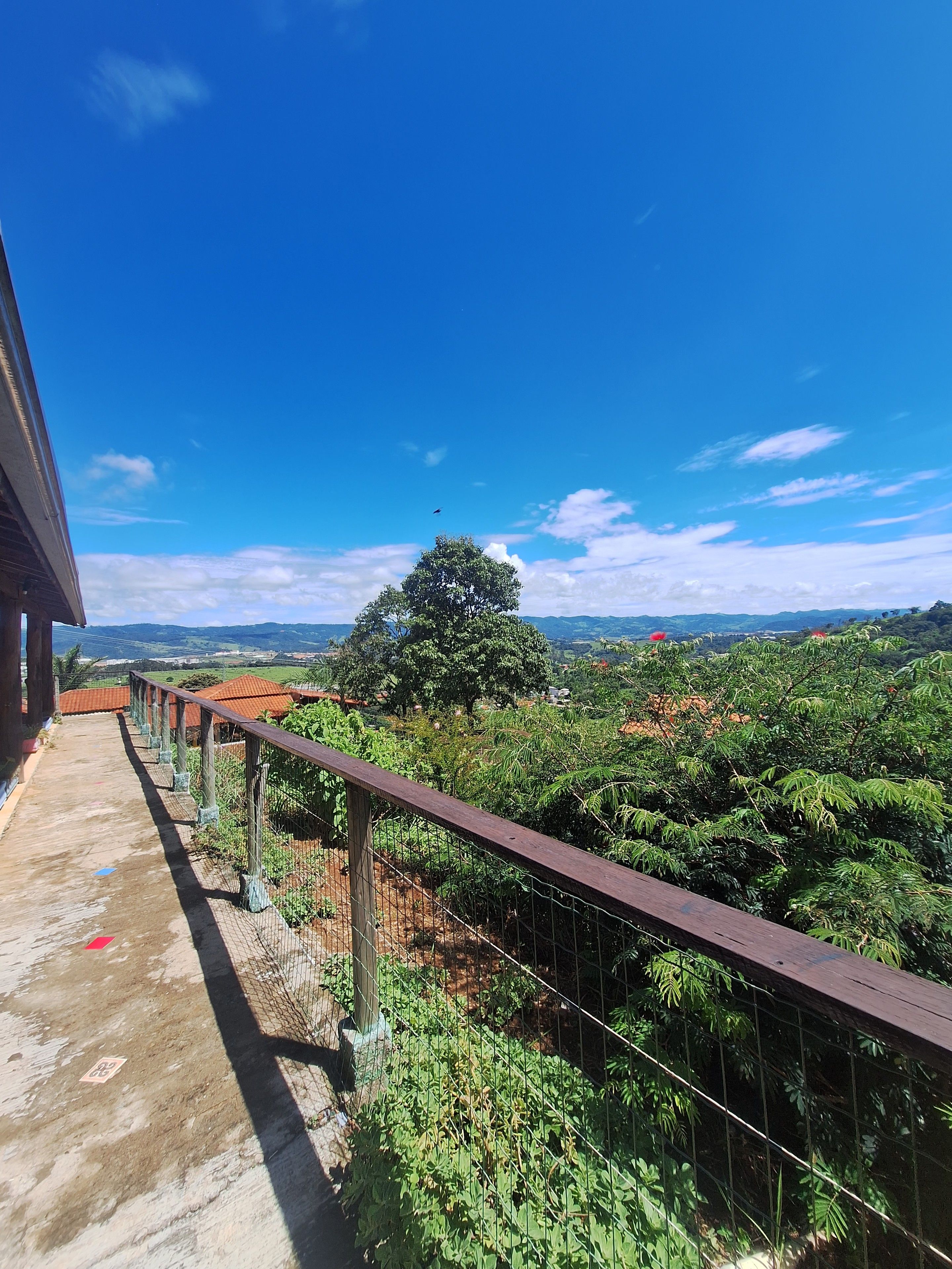 A balcony with a view of a lush landscape, a clear sky, and distant mountains.