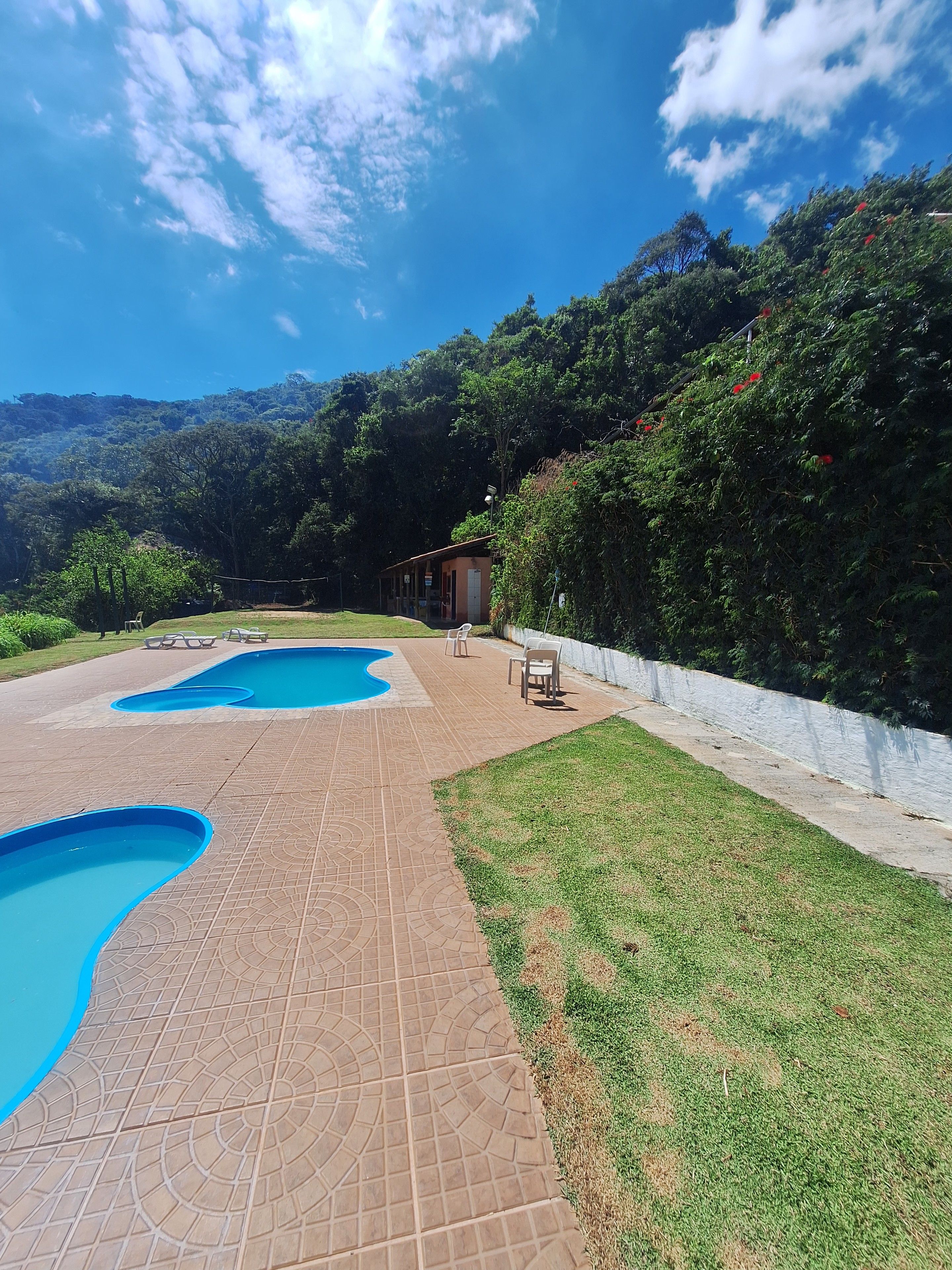 Un área de piscina con dos piscinas, una zona de estar cubierta y un edificio al fondo.