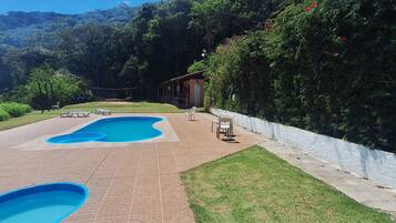 Un área de piscina con dos piscinas, una zona de estar cubierta y un edificio al fondo.