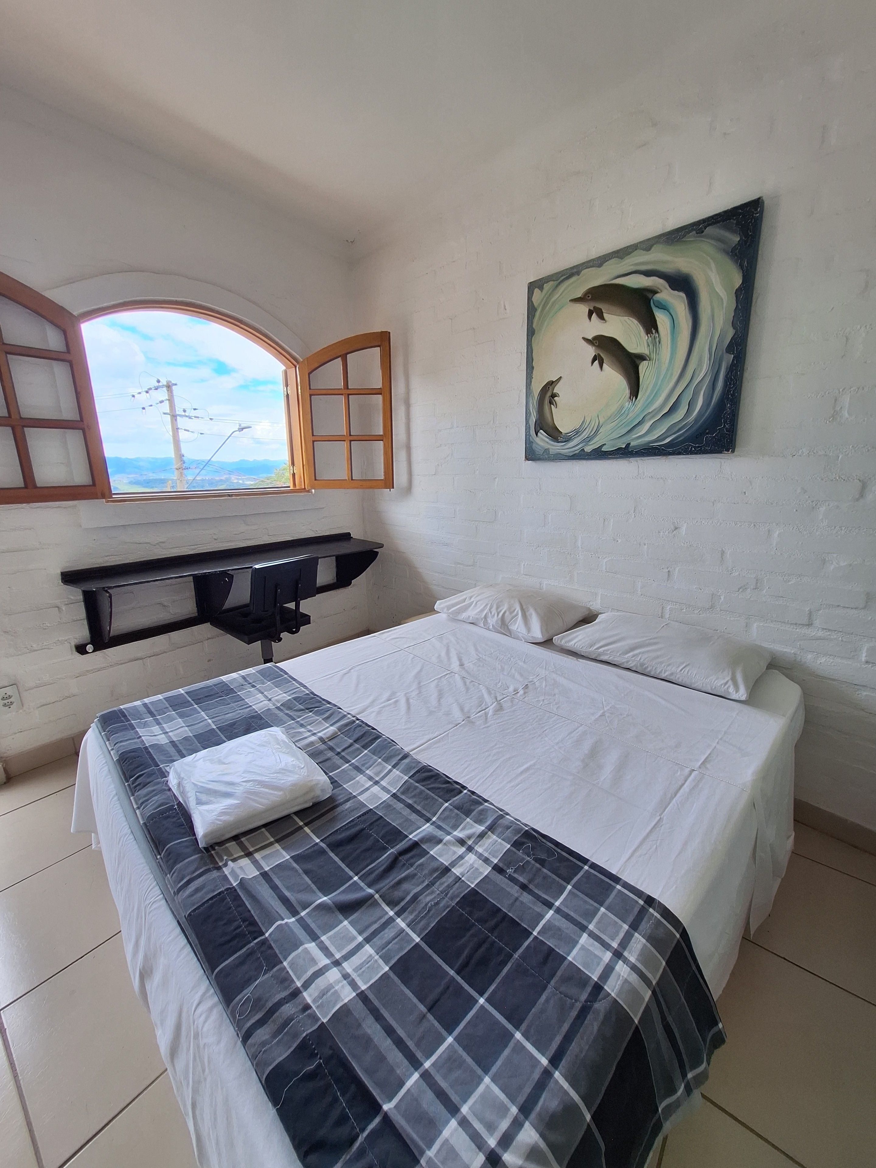 A bedroom with a bed, a painting of dolphins, a window, and a desk.