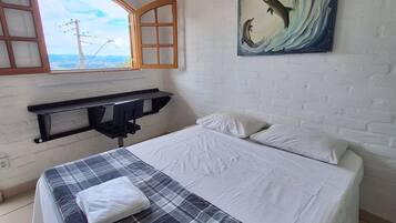 A bedroom with a bed, a painting of dolphins, a window, and a desk.