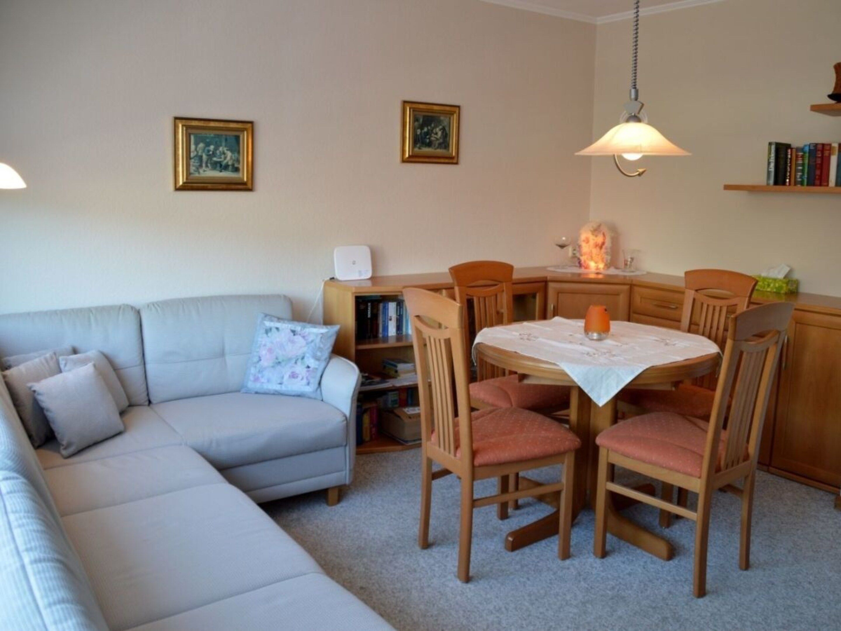 Een woonkamer met een bank, een eettafel met stoelen, een boekenkast en twee wandlampen.