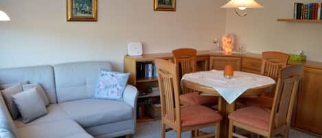 Una sala de estar con un sofá, una mesa de comedor con sillas, una estantería y dos lámparas de pared.