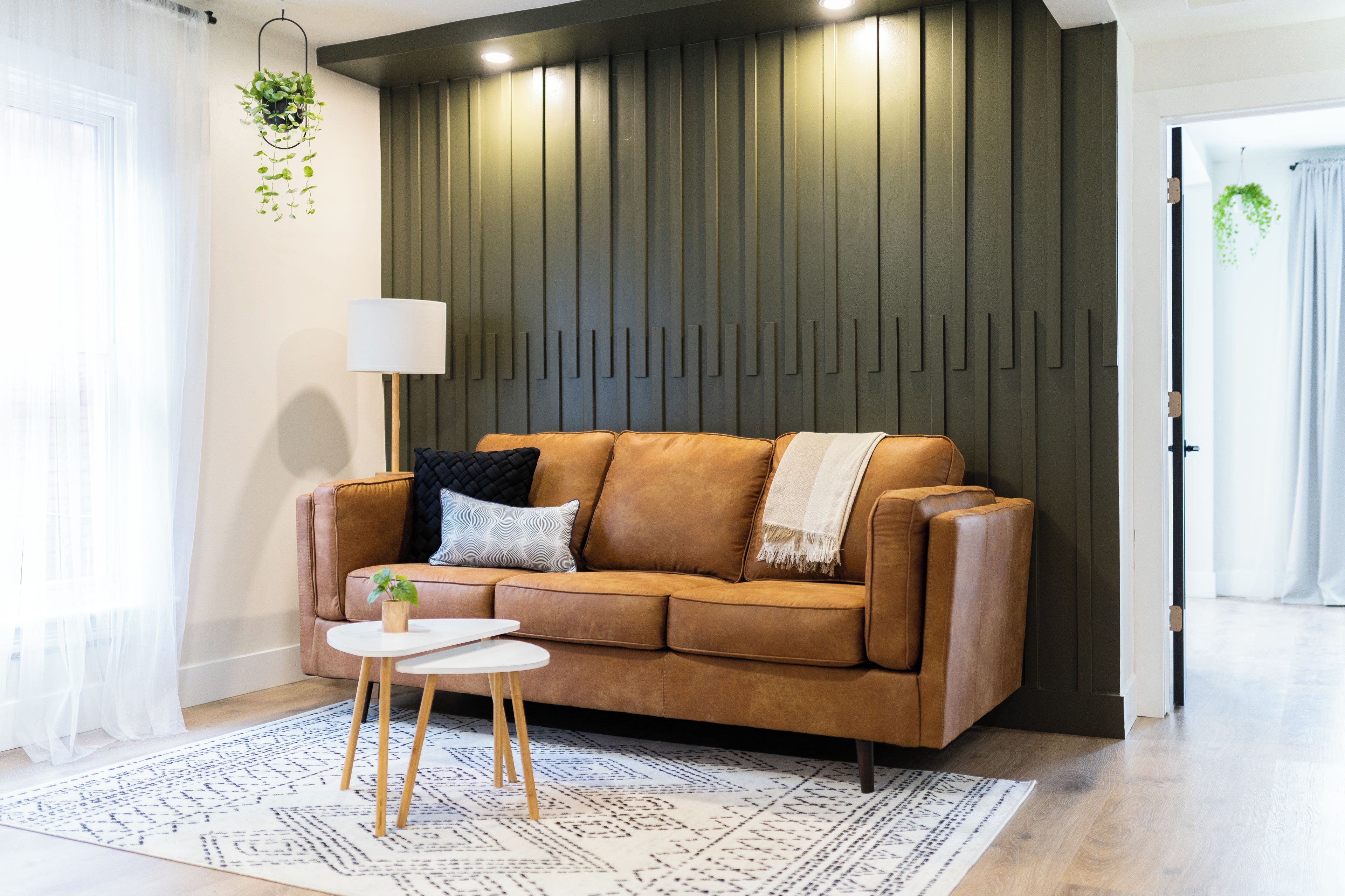 Un salon moderne avec un canapé en cuir marron, une petite table d’appoint blanche, un tapis à motifs et un mur orné de lambris en bois verticaux.