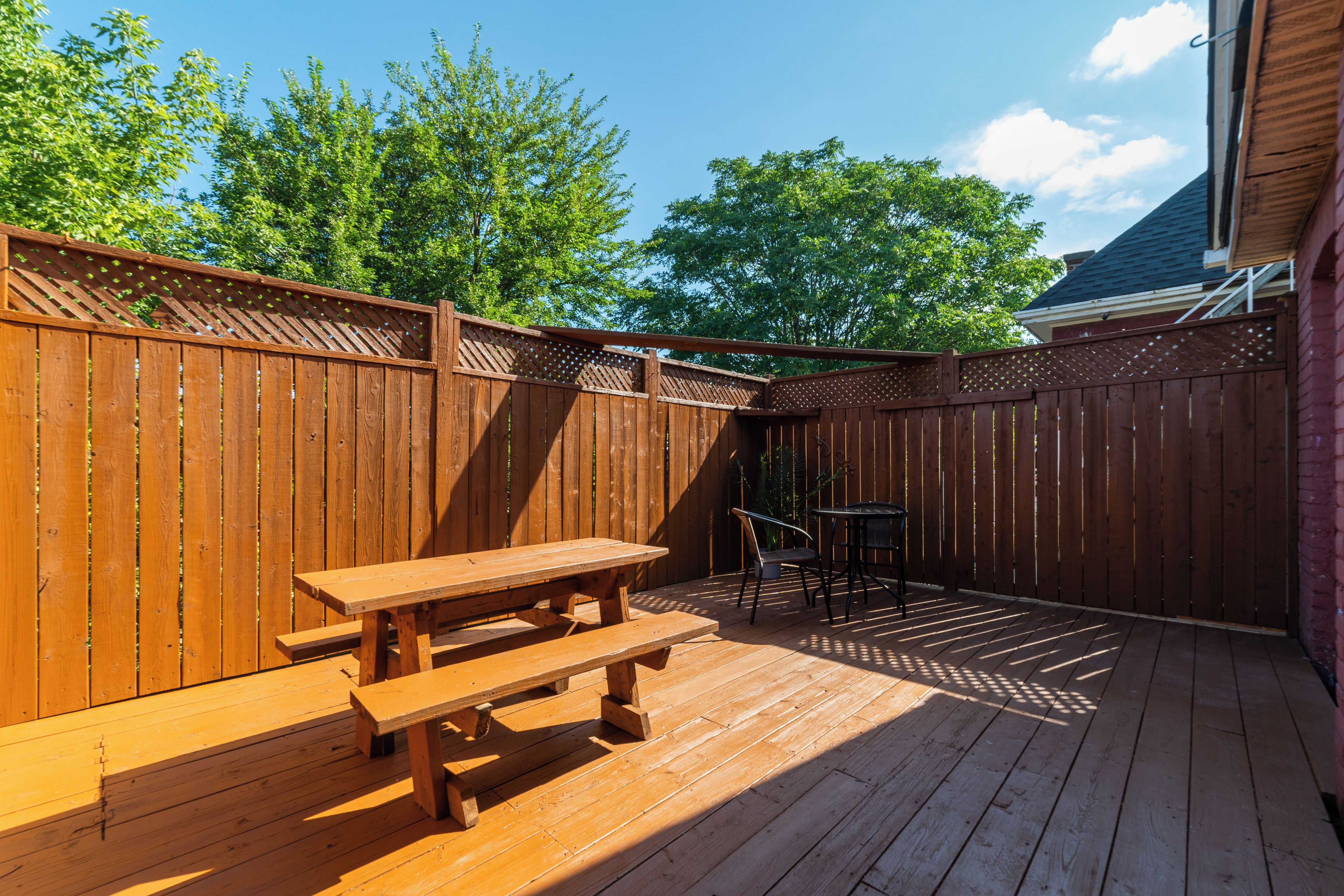 Une terrasse en bois avec une table de pique-nique et des chaises, entourée d’une clôture en bois.