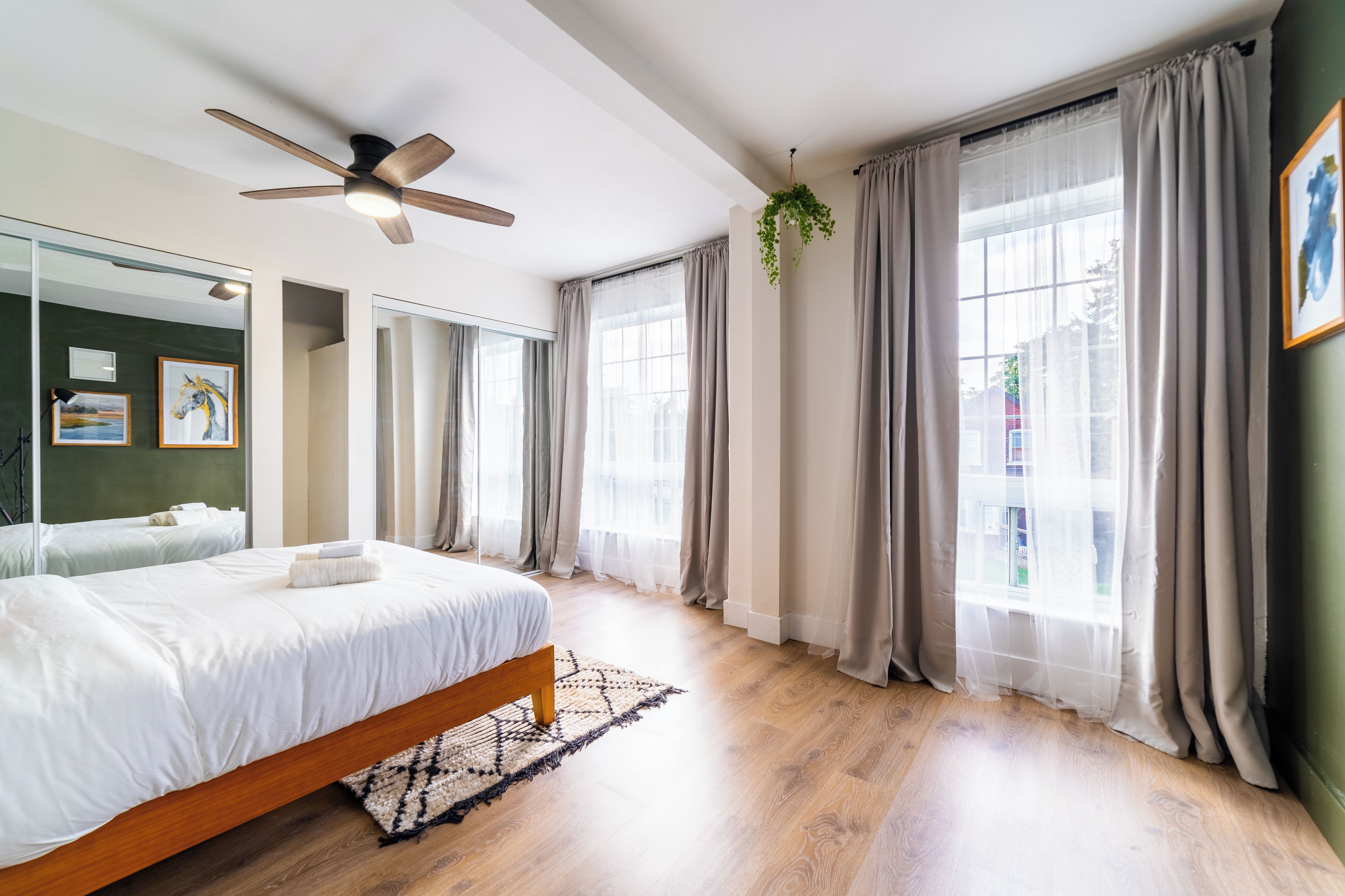 Une chambre à coucher avec un lit, un ventilateur de plafond, une fenêtre avec des rideaux et une plante fixée au mur.