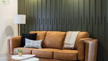 A modern living room with a brown leather sofa, a white round coffee table, and a patterned rug.