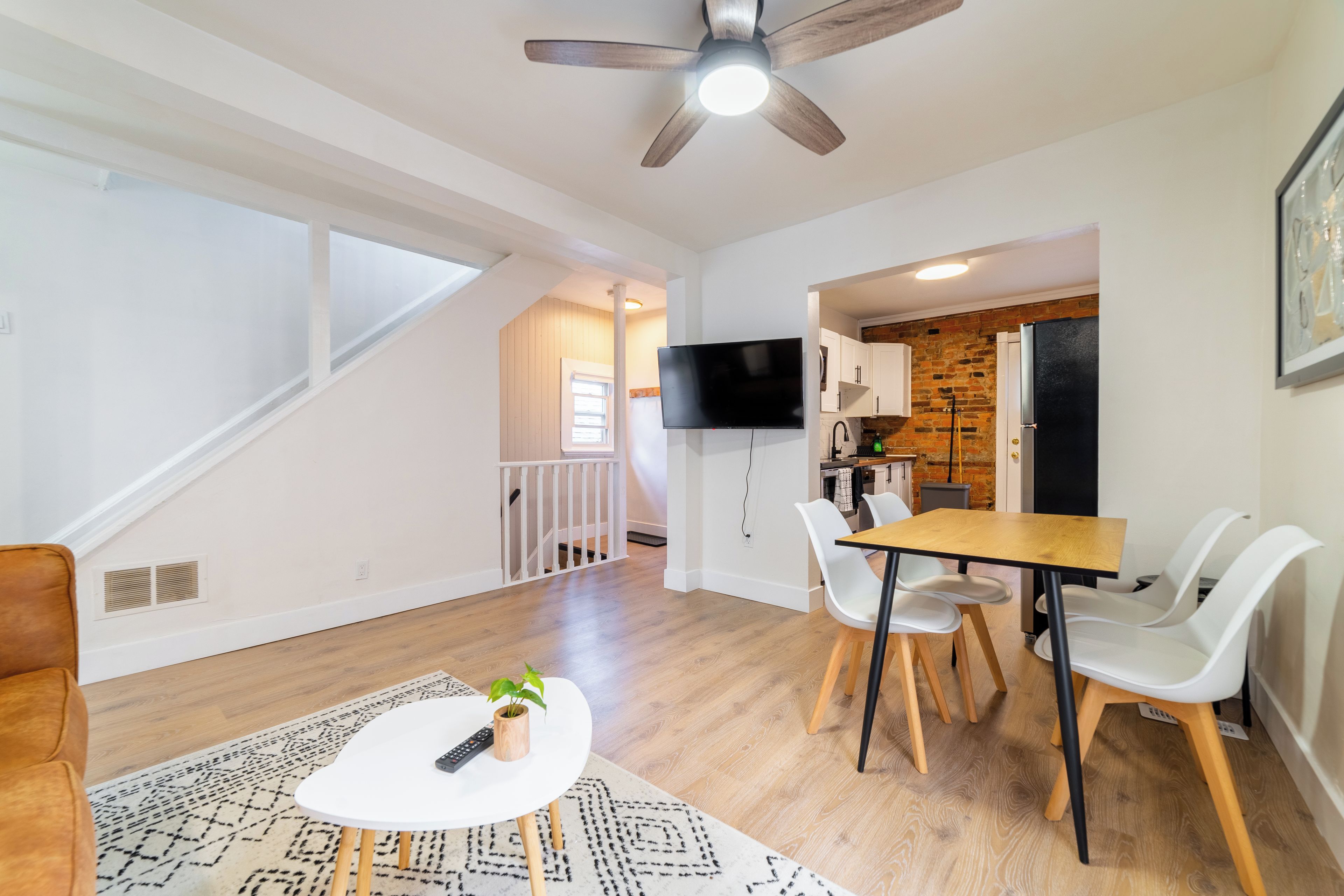 A modern living room with a dining area, a TV mounted on the wall, and a staircase leading to an upper level.