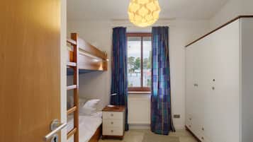 A bedroom with a bunk bed, a bedside table with a lamp, a wardrobe, and a window with curtains.