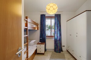 A bedroom with a bunk bed, a bedside table with a lamp, a wardrobe, and a window with curtains. - Apartment "Strandvilla-Lubmin" with Sea View, Private Terrace, and Wi-Fi (Lubmin)