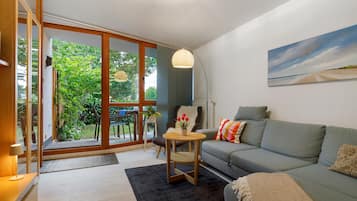 A modern living room with a grey sofa, a small round table, and a view of a garden through glass doors.