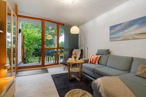Una sala de estar moderna con un sofá gris, una mesita redonda y vistas a un jardín a través de puertas de cristal.