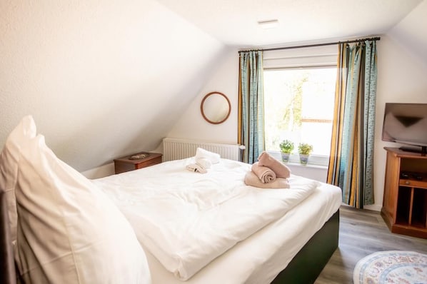 A hotel room with a bed, a nightstand, a television, and a window with curtains. - Anno 1895 Vacation Home – Historic charm meets modern living comfort! <br>Welcome to our lovingly renovated captain's house in idyllic Manslagt! The Anno 1895 vacation home can accommodate up to 5 people and combines East Frisian... (Manslagt)