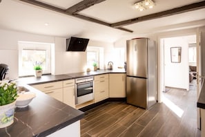 A modern kitchen with a built-in oven, a large refrigerator, and a flat-screen TV mounted on the wall. - Anno 1895 Vacation Home – Historic charm meets modern living comfort! <br>Welcome to our lovingly renovated captain's house in idyllic Manslagt! The Anno 1895 vacation home can accommodate up to 5 people and combines East Frisian... (Manslagt)