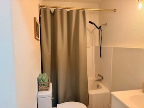 Een badkamer met douchegordijn, toilet, bad en wastafel.