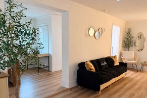 Een woonkamer met een zwarte bank, een houten salontafel en een grote potplant.