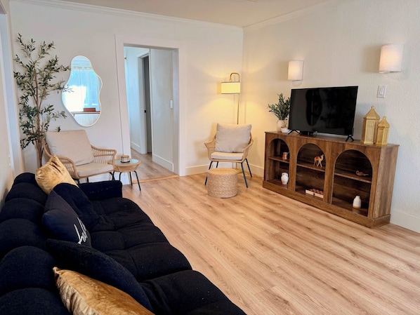 Een woonkamer met een zwarte bank, twee fauteuils, een houten tv-meubel en een spiegel aan de muur.