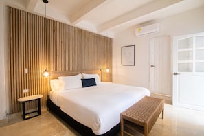 A hotel room with a bed, bedside table, wall-mounted lamp, and a door with a window. - Old City 11 Bedroom Mansion (Cartagena de Indias)