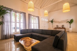 A modern living room with a sectional sofa, large windows with sheer curtains, and a wooden coffee table. - Old City 11 Bedroom Mansion (Cartagena de Indias)