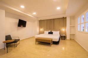 A modern bedroom with a large bed, a flat-screen TV mounted on the wall, a bench, and a chair. - Old City 11 Bedroom Mansion (Cartagena de Indias)