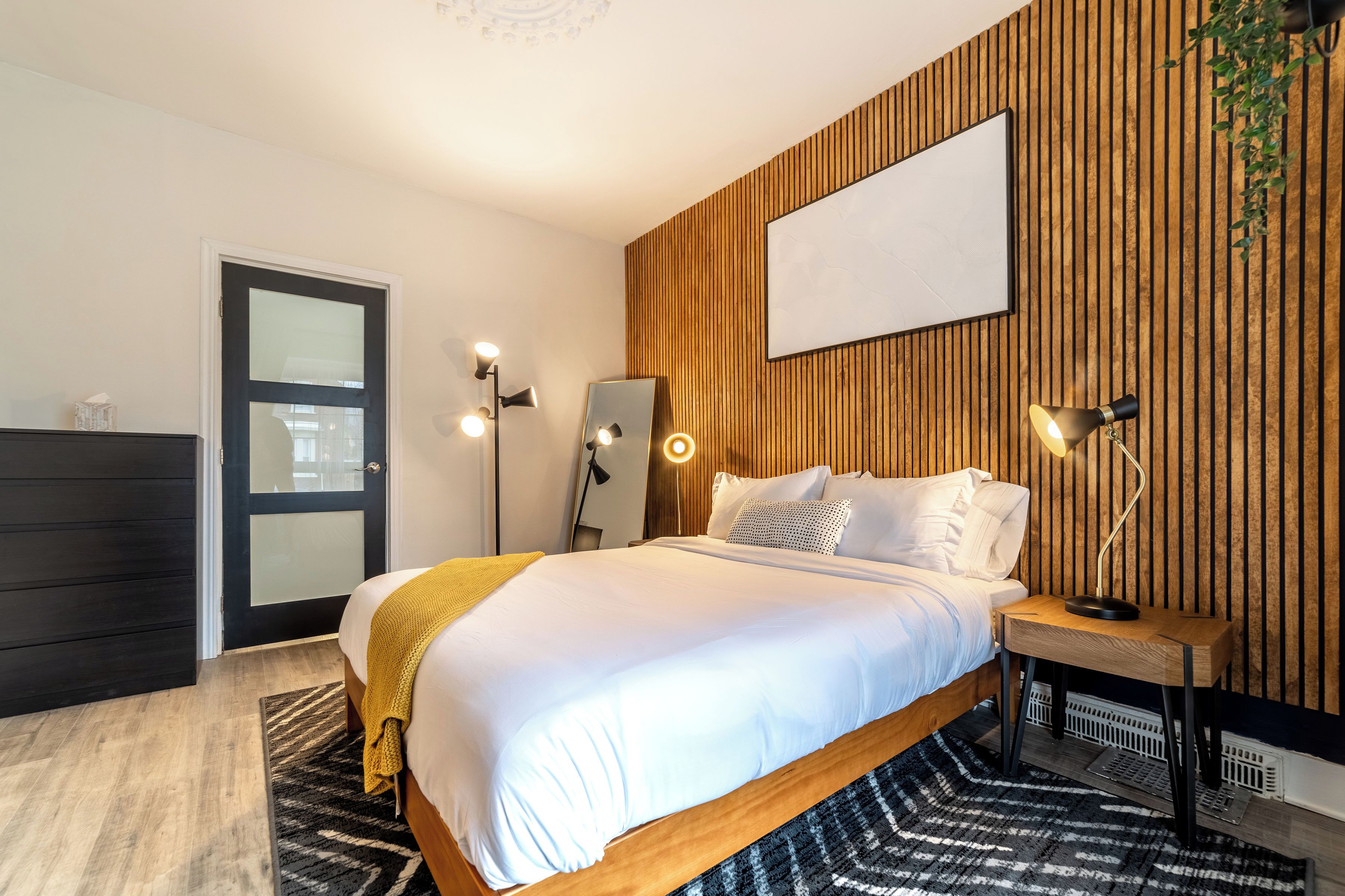 A modern bedroom with a bed, bedside lamps, a mirror, and a wooden accent wall.