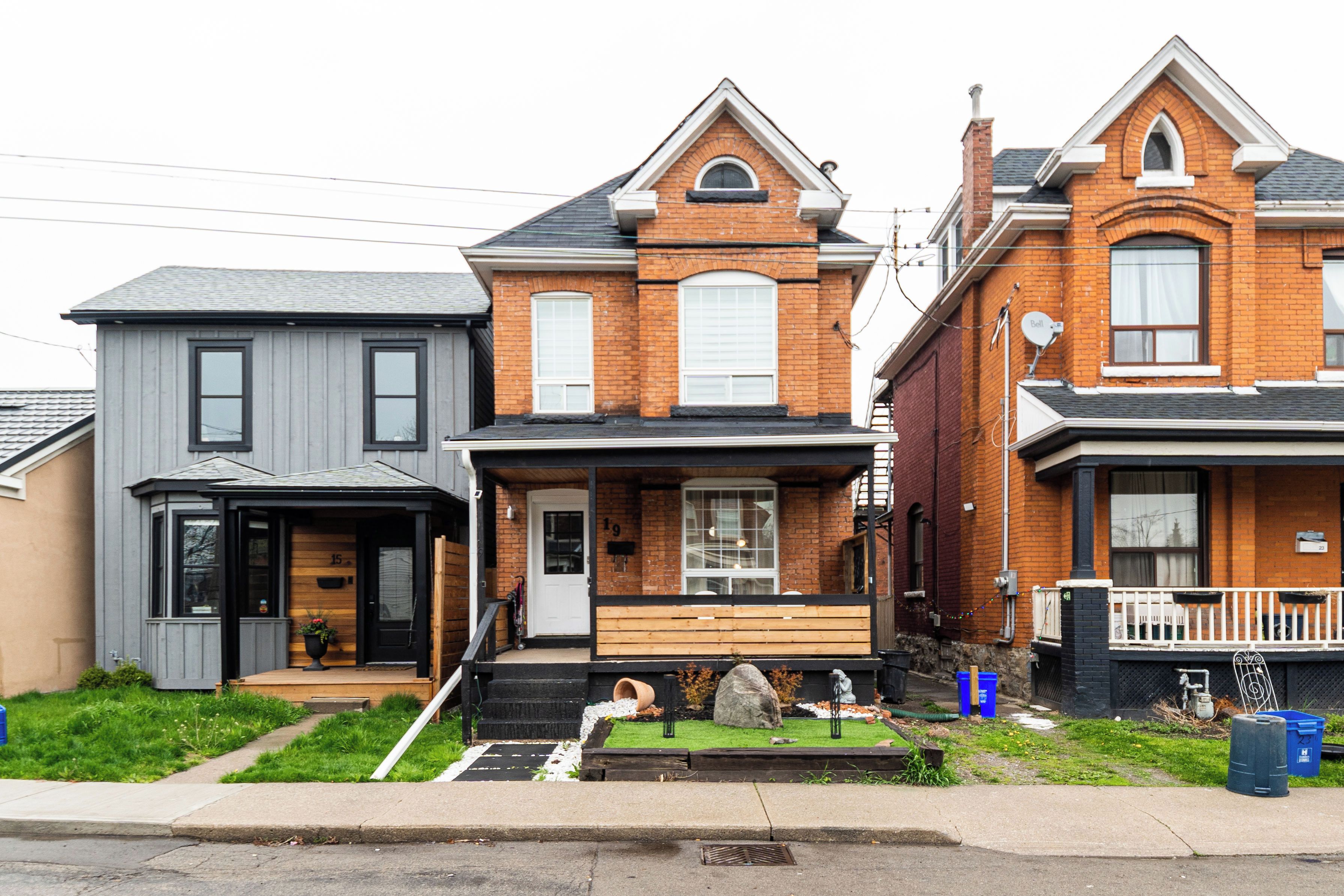 A row of three houses with distinct architectural styles, a front yard, and a sidewalk.