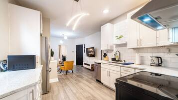A modern kitchen with white cabinetry, a black refrigerator, and a stainless steel range hood.