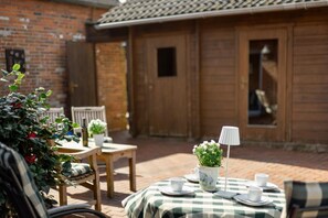 An outdoor dining area with a checkered tablecloth, chairs, a potted plant, and a lamp. - Conny's Cabin – <br>Historic charm meets modern comfort! Welcome to our lovingly restored vacation home, located right on the canal in idyllic Grimersum. Spanning 98 m&sup2;, a cozy vacation home for up to 4 people awaits you... (Krummhörn)
