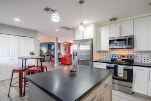 A modern kitchen with a central island, stainless steel appliances, and a dining area with red chairs. - Hidden Oasis Near Old Town with Pool & More! (Scottsdale)