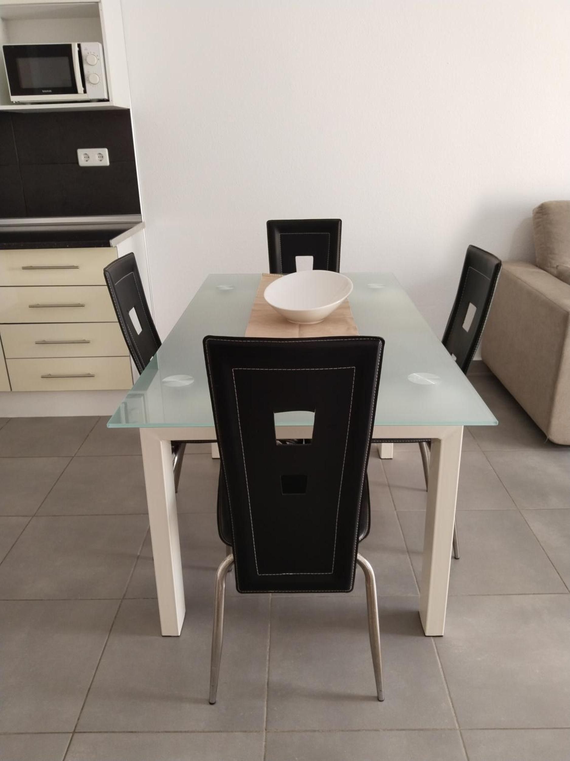 Een eetgedeelte met een tafel met glazen blad, zwarte stoelen en een witte kom op de tafel.