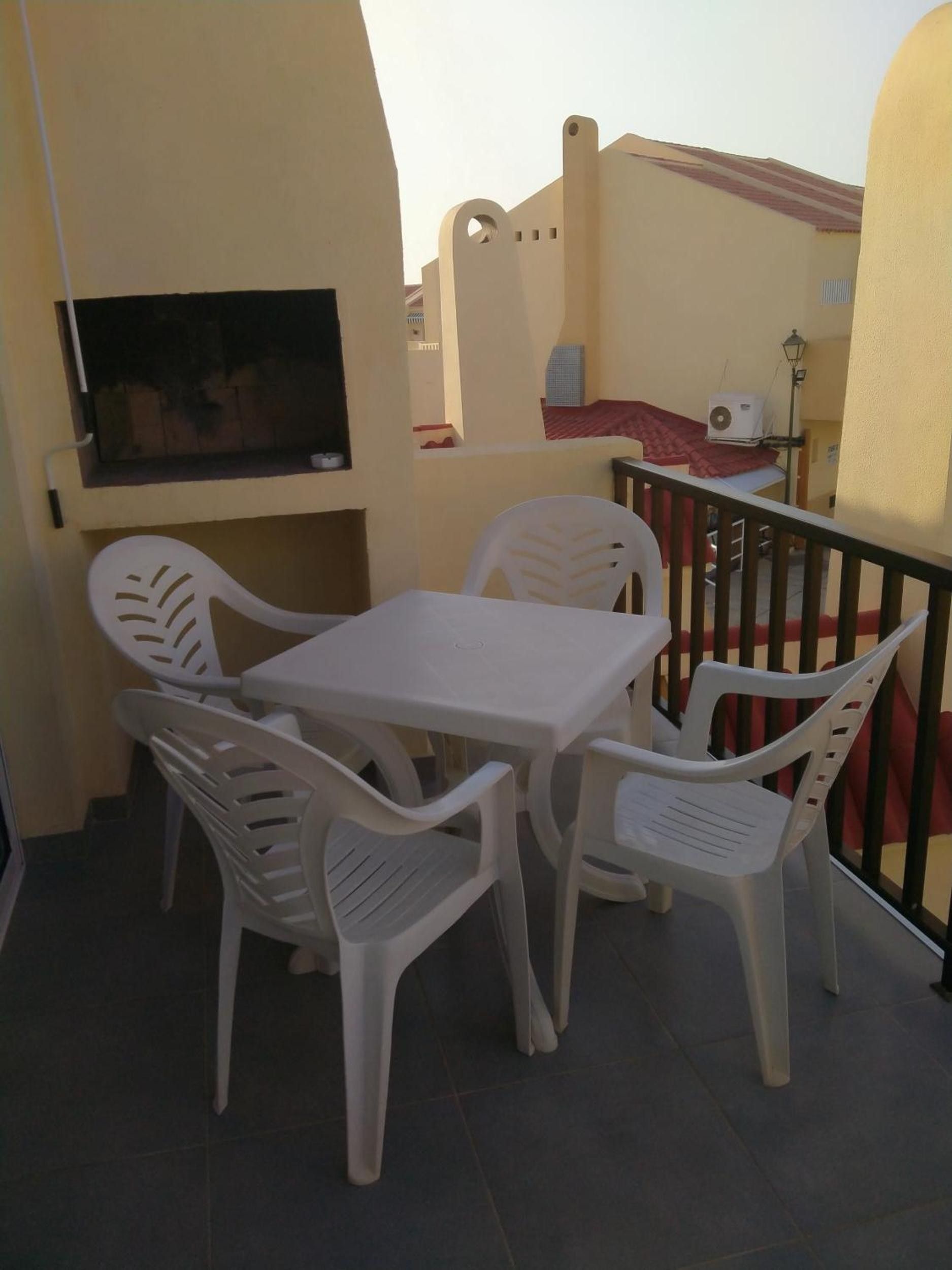 Een balkon met een tafel en stoelen, een aan de muur bevestigde televisie en een leuning.