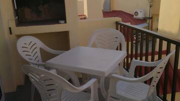 Een balkon met een tafel en stoelen, een aan de muur bevestigde televisie en een leuning.