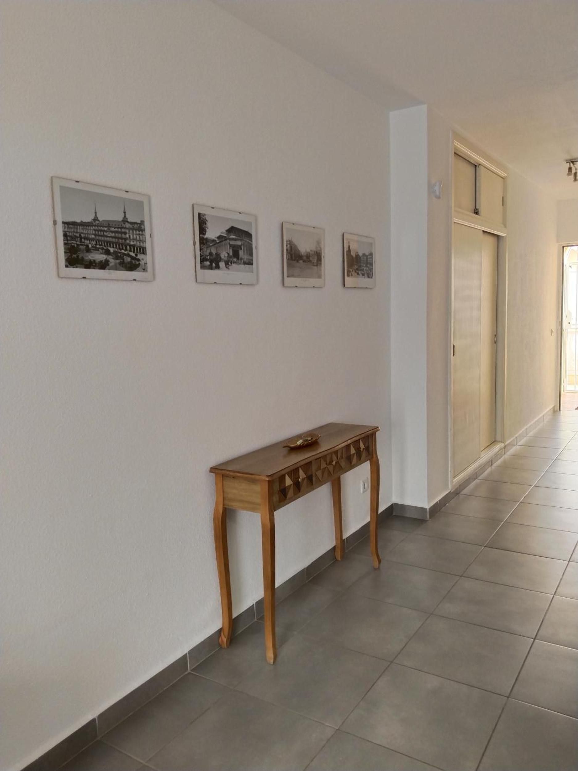 Un couloir avec une console en bois et quatre photographies encadrées accrochées au mur.