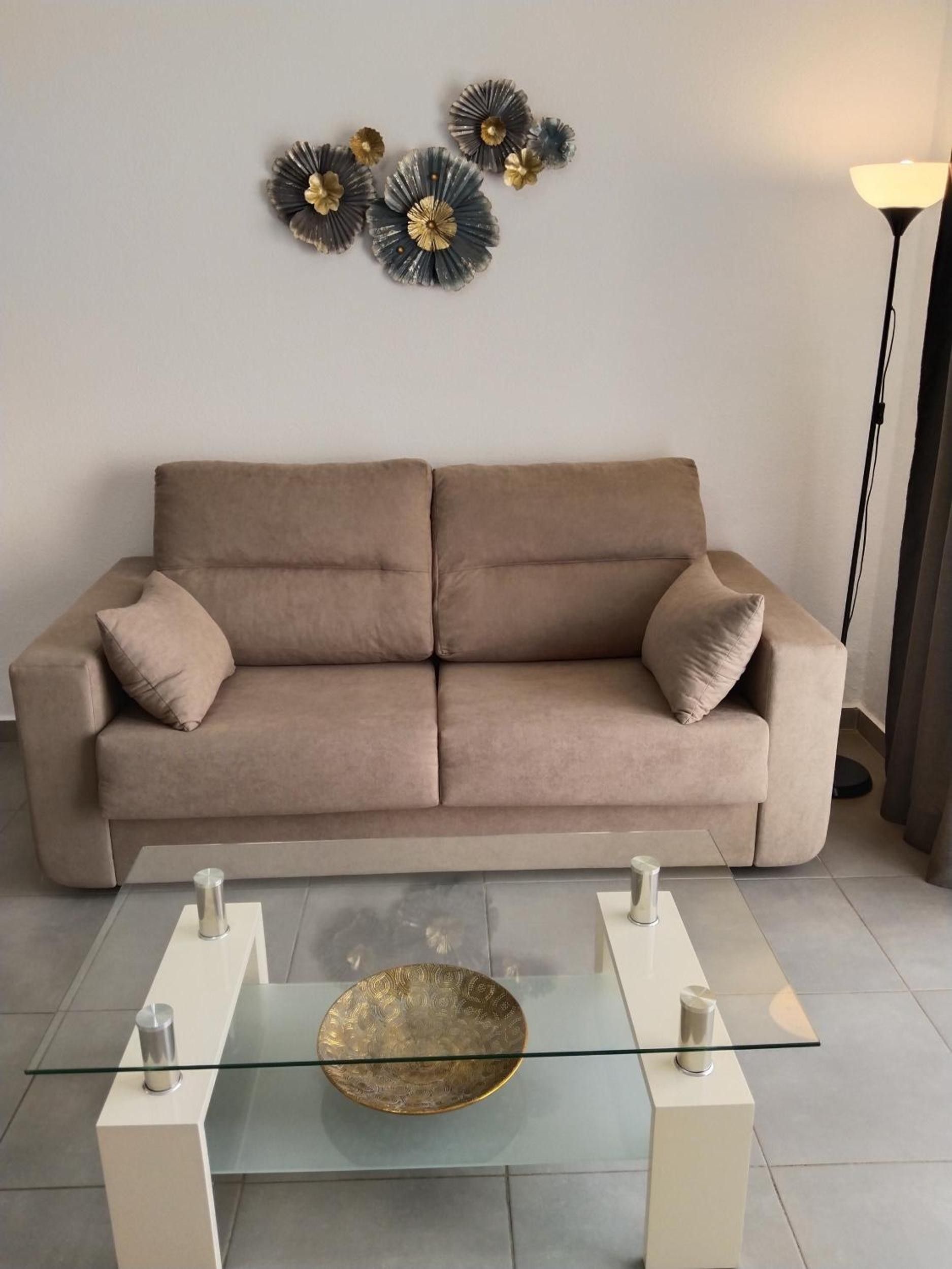 Un salon moderne avec un canapé beige, une table basse en verre agrémentée d’objets décoratifs et des œuvres d’art murales.