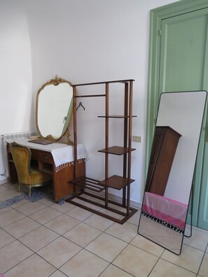 A room with a vanity, a mirror, a wooden shelf unit, and a bed with a pink and white striped blanket. - New Listing (Palermo)