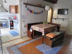 Quarto com cama, mesa, espaço de cozinha e TV fixada na parede.