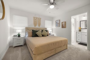 A bedroom with a bed, nightstands, a ceiling fan, and a bathroom visible through an open door. - 2BR · 2 Bath · Golf Cart · Mins to Eastport Sq (Sumterville)